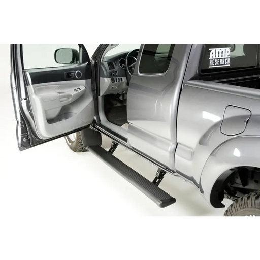 Silver truck with open door featuring AMP Research 2005-2015 Toyota Tacoma Double Cab PowerStep - Black.