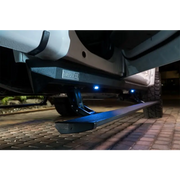 AMP Research 18-24 Jeep Wrangler JL 2DR PowerStep XL with OEM Style Illumination - Black, showing car with light on side.