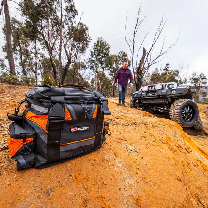 Man carrying a large black and orange bag on a dirt road for ARB Premium Recovery Kit S2.