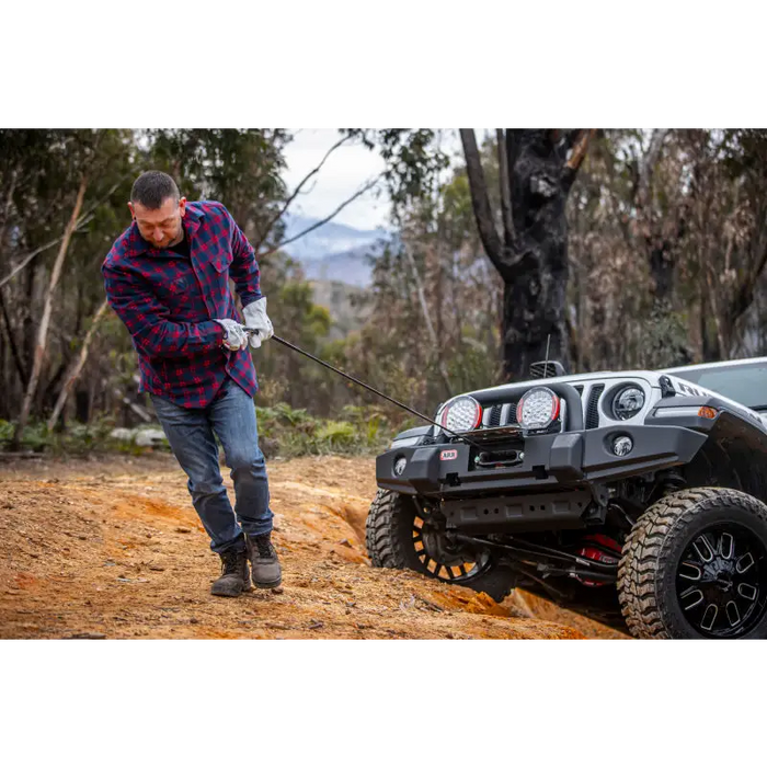 Man using ARB Premium Recovery Kit S2 snatch strap to pull toy car on dirt road