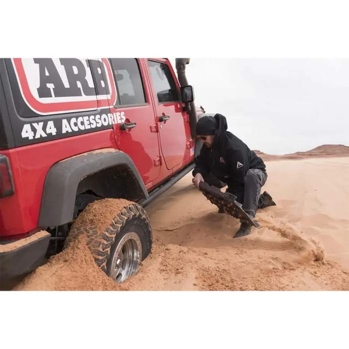 Man digging at sand in a jeep with ARB Tred Pro Green recovery board