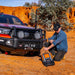 Man kneeling next to red pick truck with ARB Weekender Recovery Kit in the background.