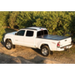 White truck parked in dirt next to BAK 05-15 Toyota Tacoma truck bed cover.