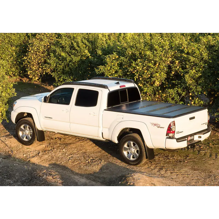 White Toyota Tacoma truck parked in front of bush - BAKFlip G2 truck bed cover.