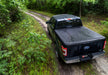 Black truck driving down dirt road with bak 2021+ ford f-150 revolver x4s 6.5ft bed cover