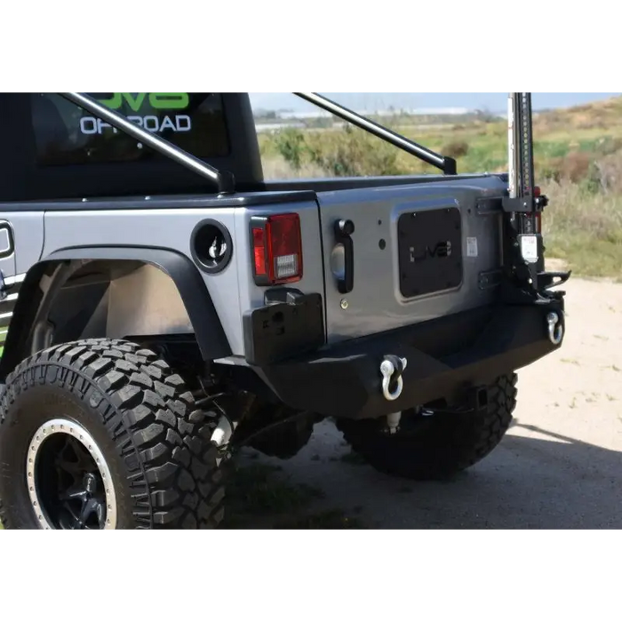 DV8 Offroad 07-18 Jeep Wrangler JK Steel Mid Rear Bumper parked on dirt with large tire