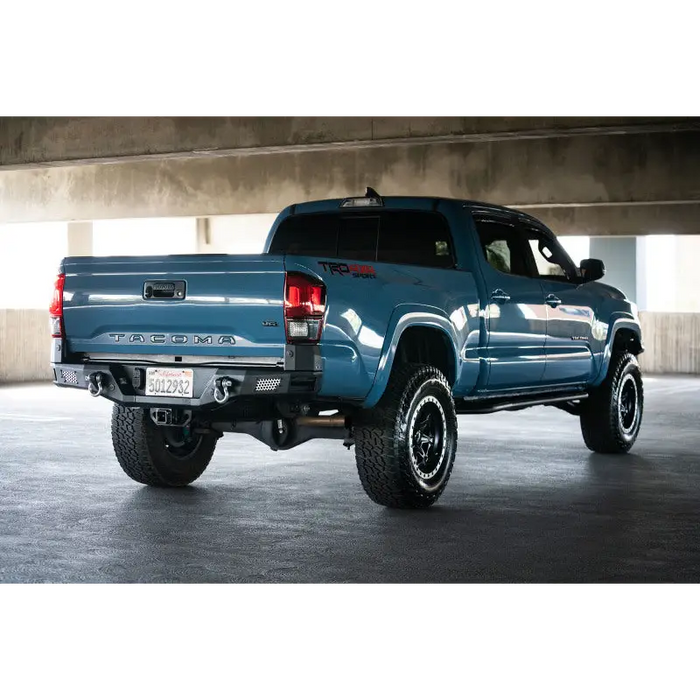 Blue truck parked in parking garage next to DV8 Offroad 16-23 Toyota Tacoma MTO Series rear bumper.