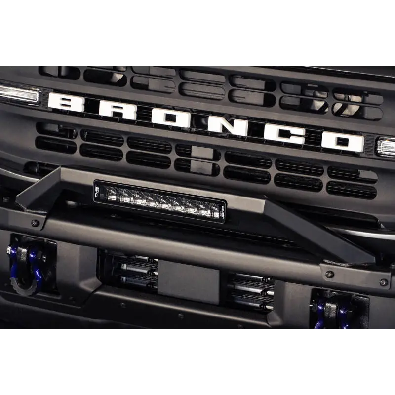 Close up of DV8 Offroad 21-22 Ford Bronco Factory Modular Front Bumper Bull Bar with chrome grille and blue light.