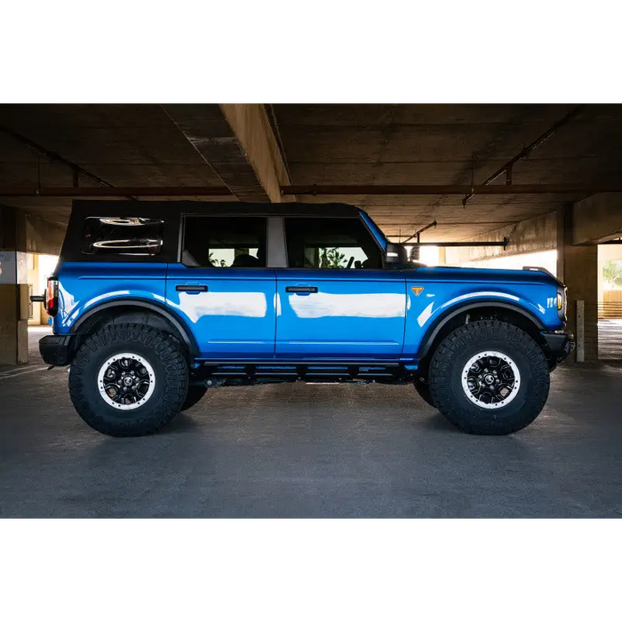 Blue truck parked in garage with large tire next to DV8 Offroad 21-22 Ford Bronco FS-15 Series Rock Sliders