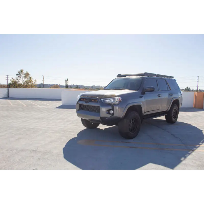 Silver Toyota SUV parked in a parking lot next to a Go Rhino 10-23 Toyota 4Runner Ceros Low Profile Roof Rack - Tex. Blk.