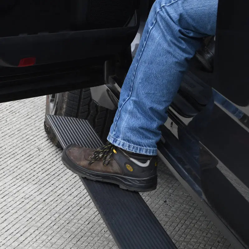 Man in jeans and boots stepping on electric running board step in Go Rhino 2024 Toyota Tacoma DC 4dr E1 Electric Running Board Kit.