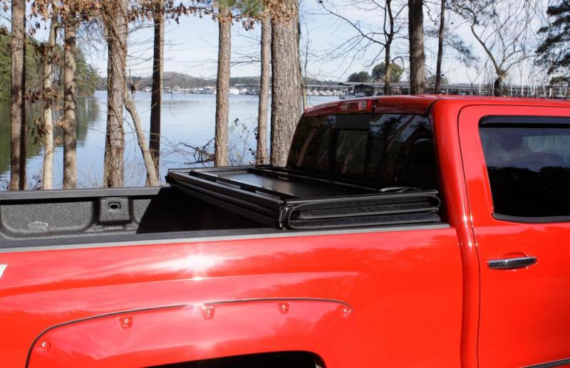 Red truck parked by lake featuring lund 05-15 toyota tacoma hard fold tonneau cover in black