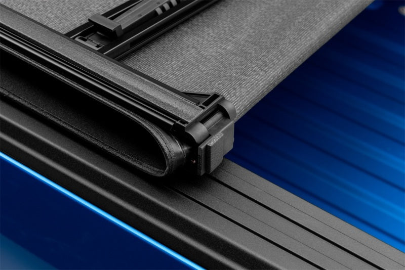 Close up of genesis elite tri-fold tonneau cover black door handle on blue car