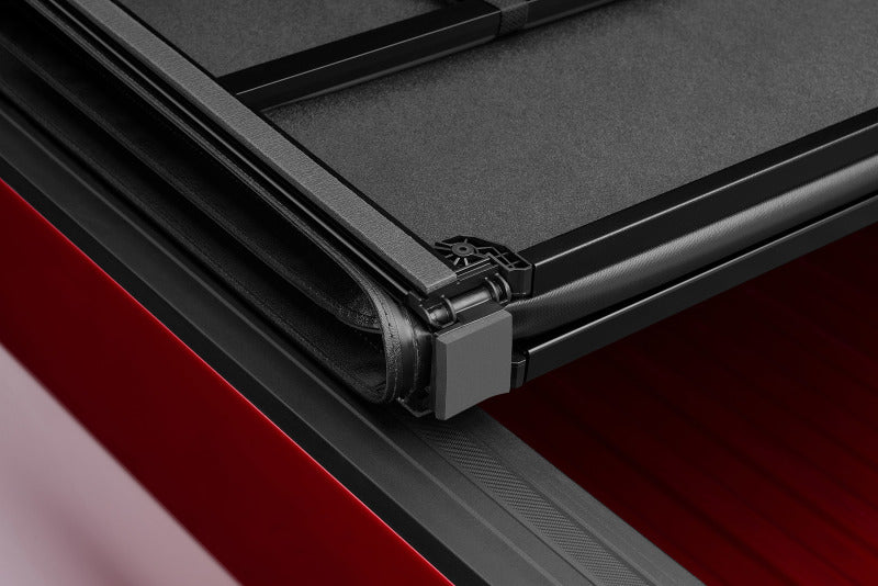 Side view of lund 16-23 toyota tacoma hard fold tonneau cover - black on red car