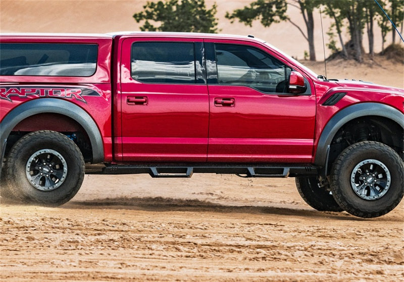 Red truck driving through dirt field next to n-fab epyx 07-18 jeep wrangler jk 4dr suv - cab length - tex. Black