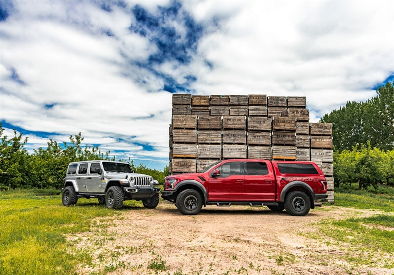Two red trucks parked in front of a wooden cabin - n-fab epyx wrangler jk 4dr suv cab length in tex. Black