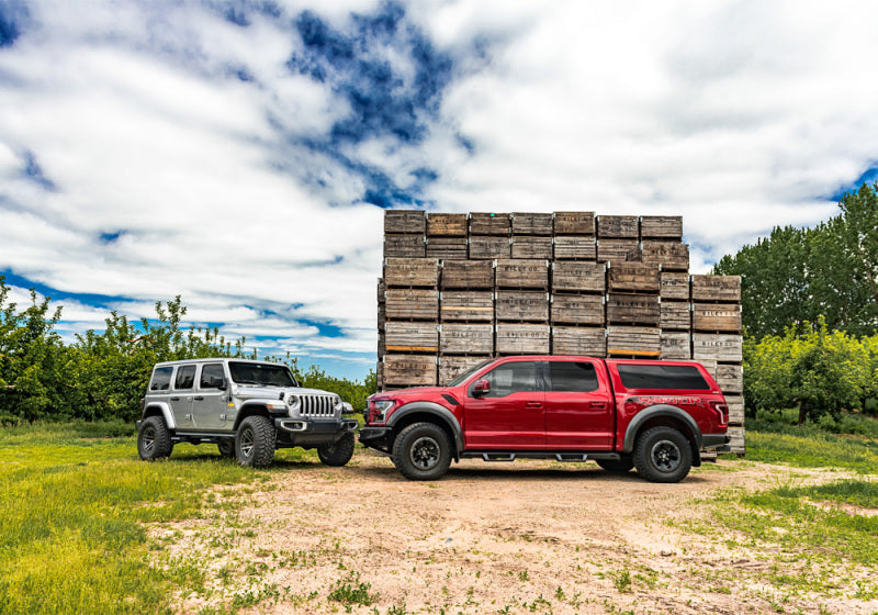 Two red trucks parked in front of a wooden cabin in n-fab epyx 07-18 jeep wrangler jk 4dr suv - cab length -