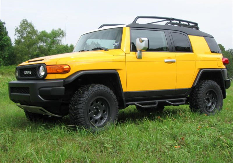 Yellow toyota fj cruiser suv with n-fab nerf steps parked in field