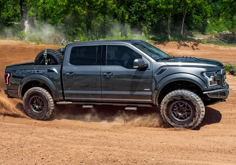 Gray truck driving on dirt through woods, showcasing n-fab rkr rails for toyota fj cruiser