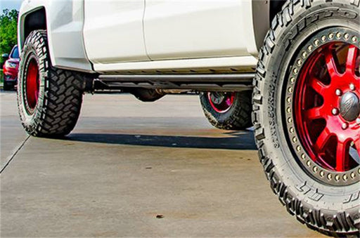 White truck with red wheels and tires featuring n-fab fab rock rails for toyota tacoma