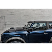 Blue Land Rover parked in front of brick wall next to Oracle 2021+ Ford Bronco Integrated Windshield Roof LED Light Bar System.