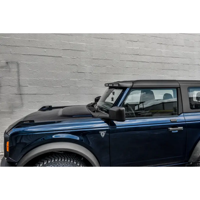 Blue Land Rover parked in front of brick wall next to Oracle 2021+ Ford Bronco Integrated Windshield Roof LED Light Bar System.