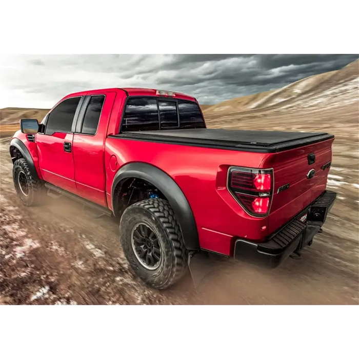 Red truck driving down dirt road with Truxedo 05-15 Toyota Tacoma 5ft Lo Pro Bed Cover.